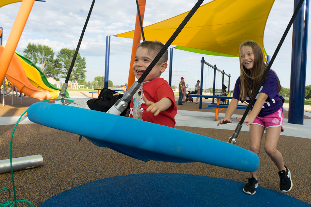 Older sister pushing younger brother on round swing